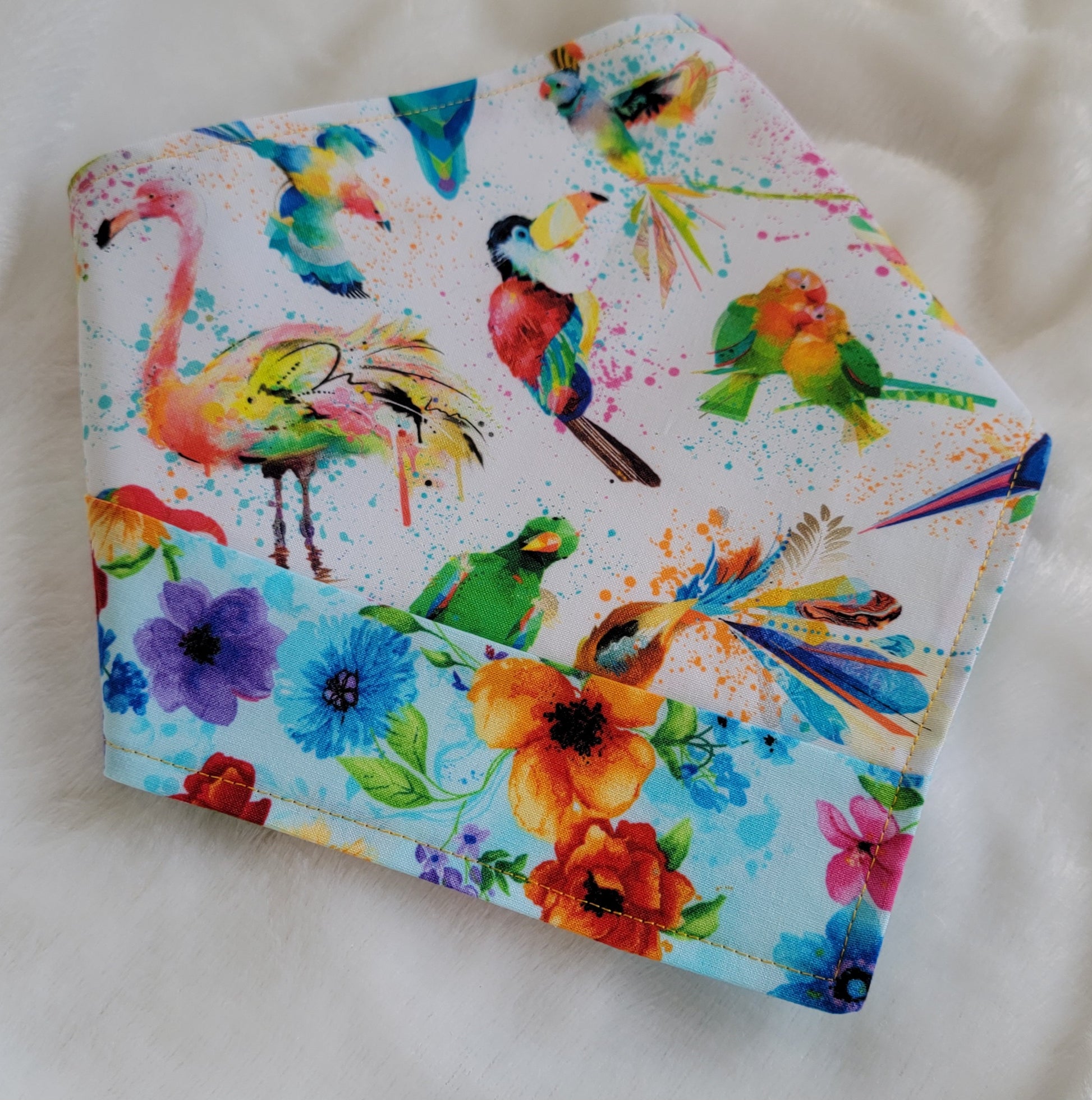 Handmade bandana featuring colorful tropical birds and floral prints patched together in stripes, unique on each side. Displayed with the corners folded under, on a white background.