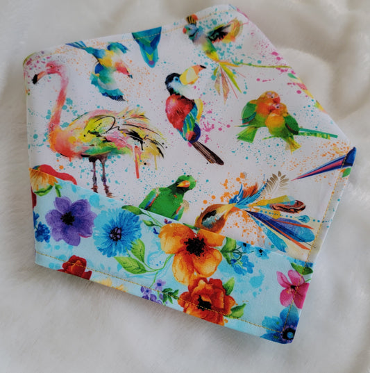 Handmade bandana featuring colorful tropical birds and floral prints patched together in stripes, unique on each side. Displayed with the corners folded under, on a white background.