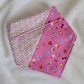 Handmade pet bandana featuring stripes of fabric with lilac scallop pattern and bright pink with cute summer motifs including umbrellas, ice cream, sunglasses, dolphins and more. Showing side with wider edge stripe of bright pink, corners are folded under and top edge is folded over to show the reverse side.