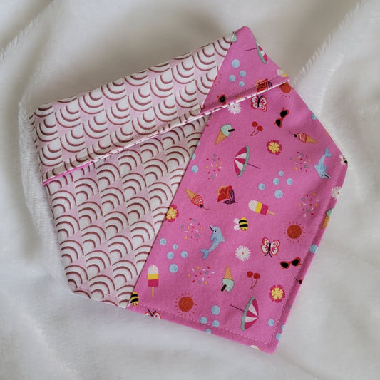 Handmade pet bandana featuring stripes of fabric with lilac scallop pattern and bright pink with cute summer motifs including umbrellas, ice cream, sunglasses, dolphins and more. Showing side with wider edge stripe of bright pink, corners are folded under and top edge is folded over to show the reverse side.