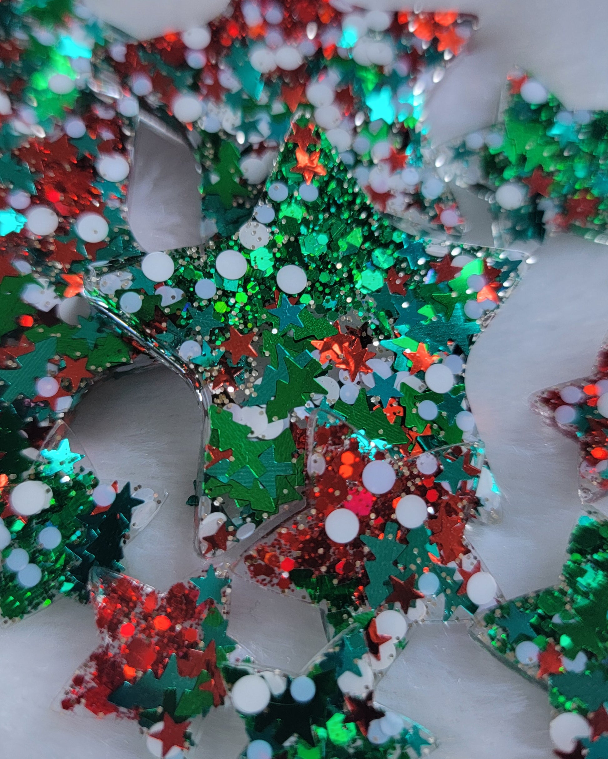 Array of star shaped epoxy resin pieces filled with red, green, and Christmas themed glitter, displayed on a white background.