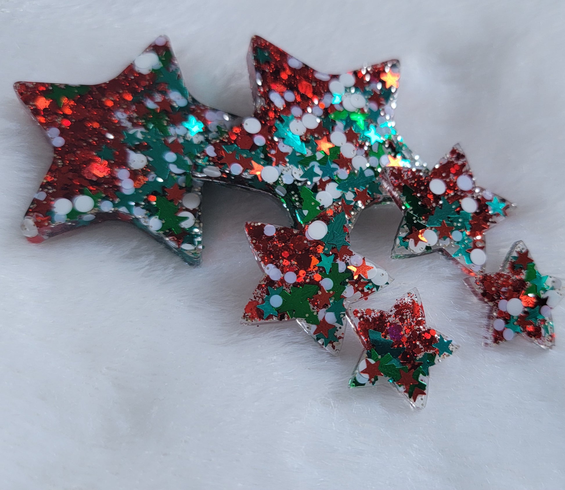 Six star shaped epoxy resin pieces filled with red and Christmas themed glitter, displayed on a white background.