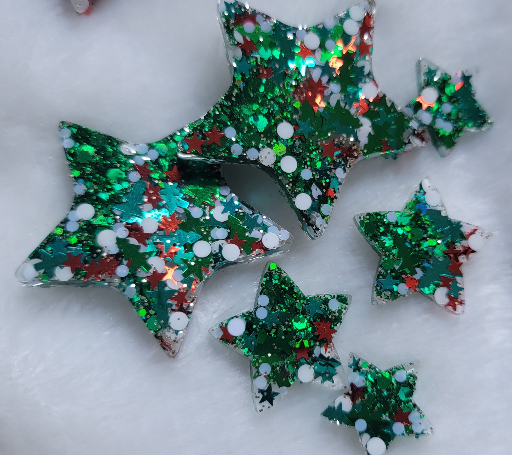 Six star shaped epoxy resin pieces filled with green and Christmas themed glitter, displayed on a white background.