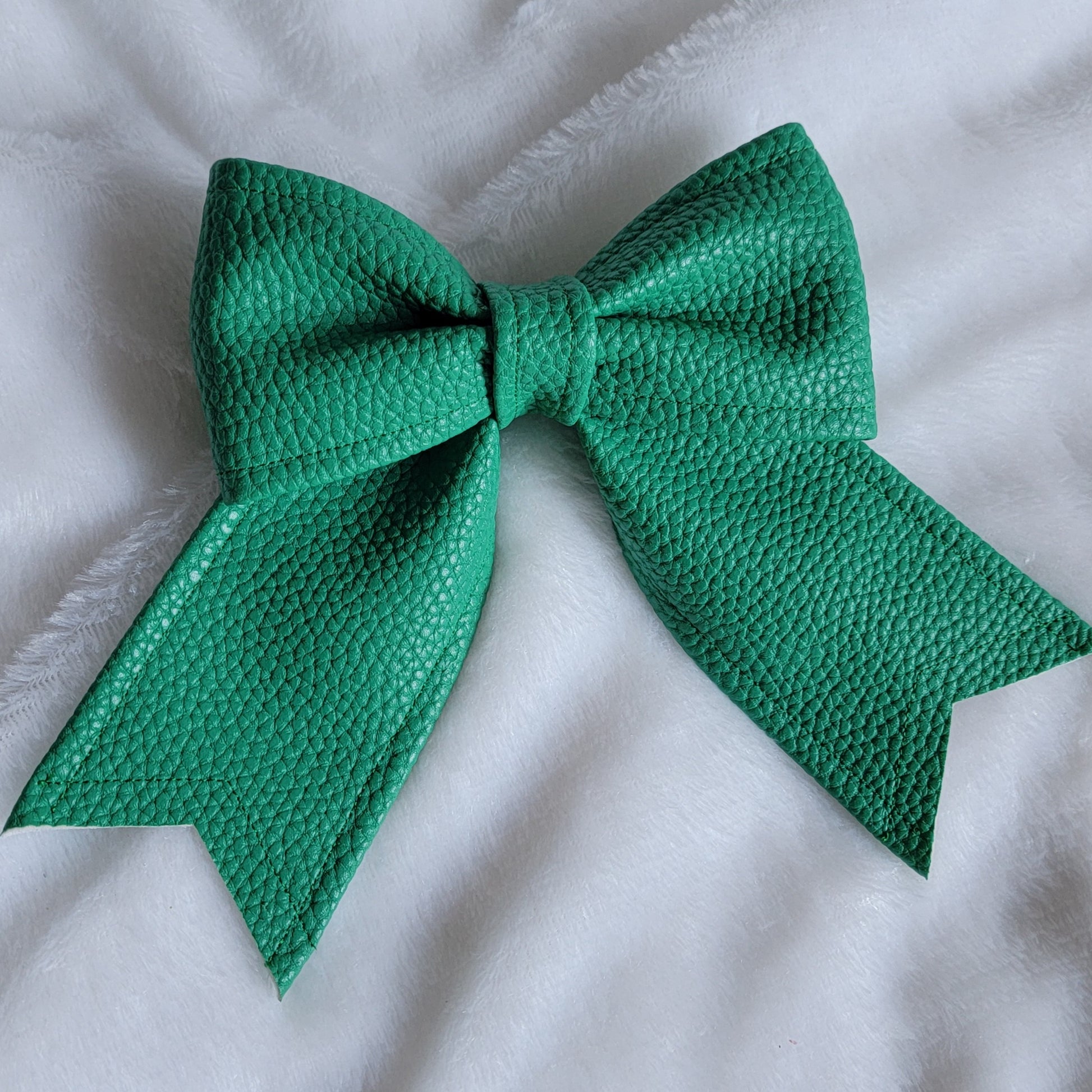 Green faux leather sailor bow displayed on a white fabric background.