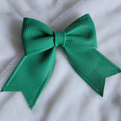Green faux leather sailor bow displayed on a white fabric background.