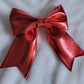 Red metallic faux leather sailor bow displayed on a white fabric background.