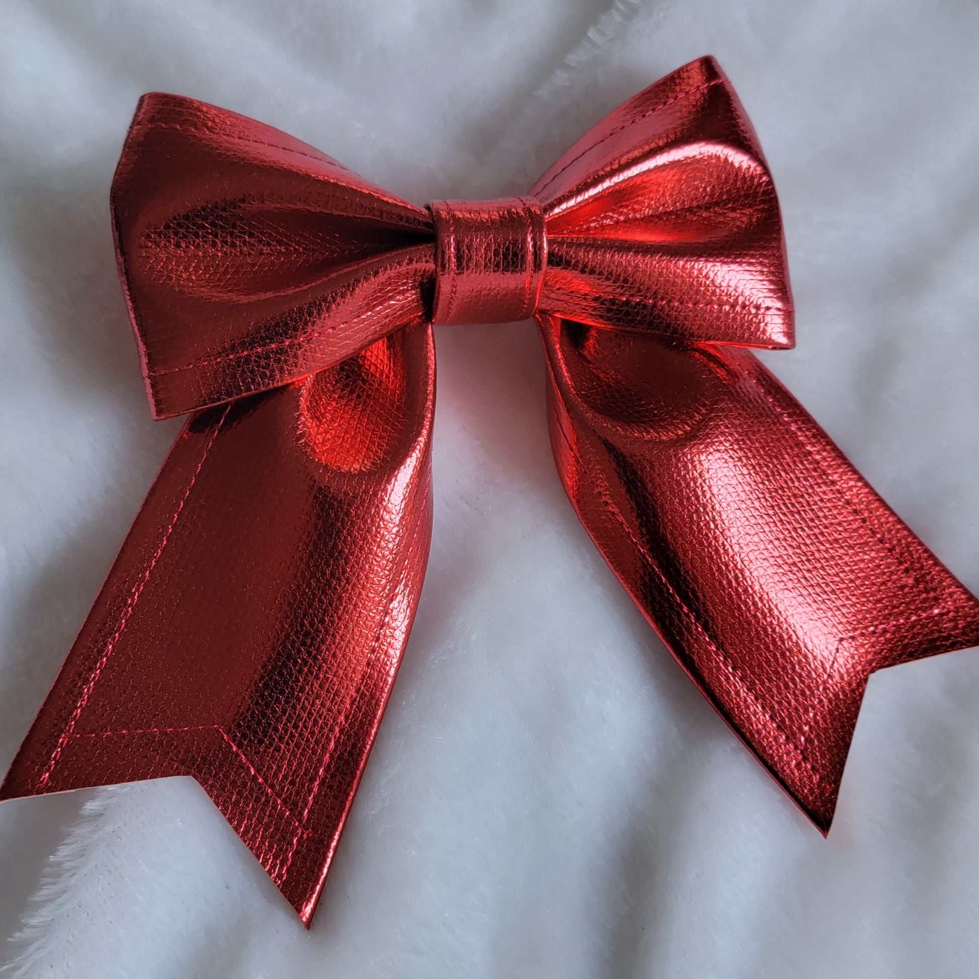 Red metallic faux leather sailor bow displayed on a white fabric background.