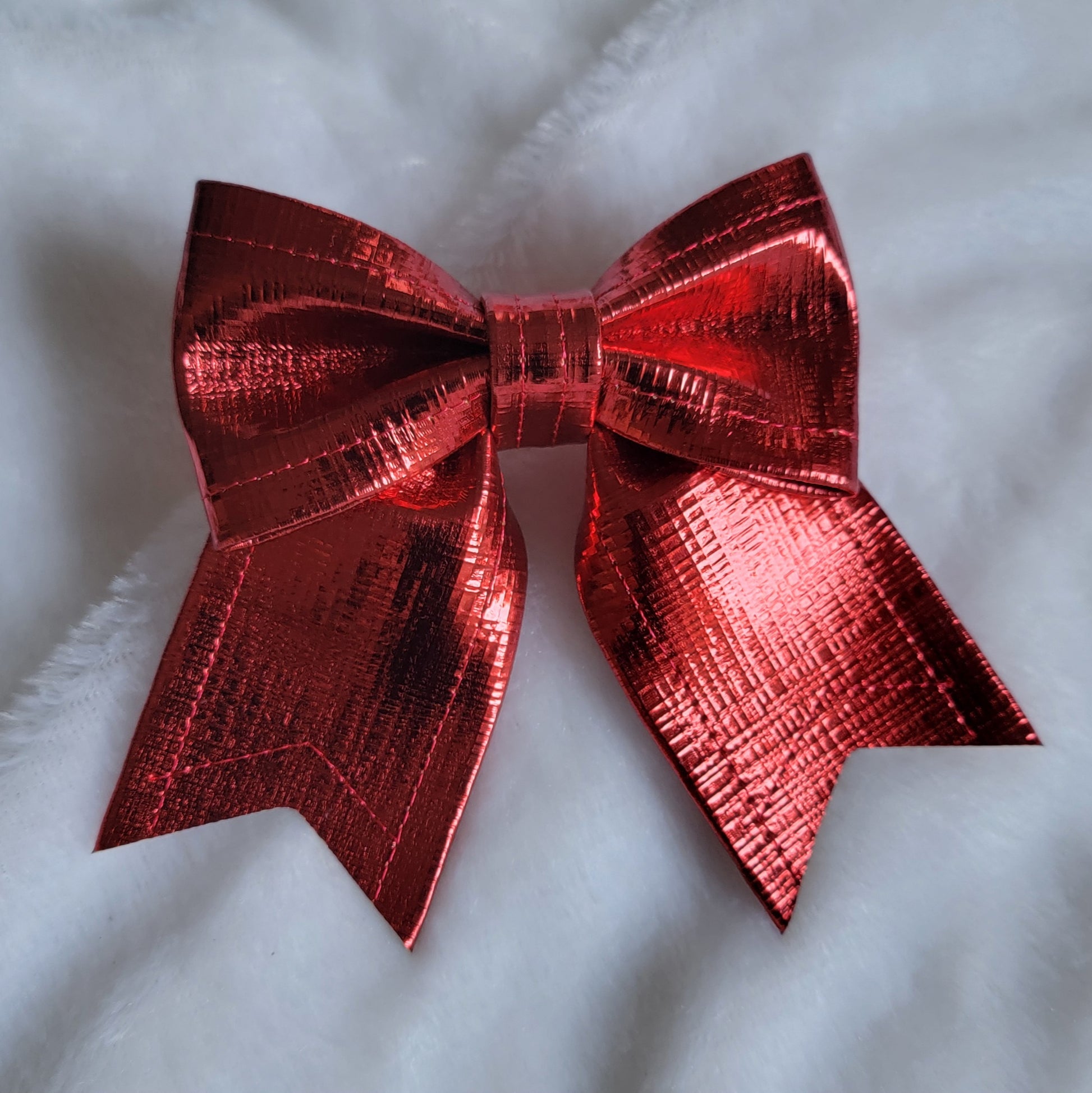 Red metallic faux leather sailor bow displayed on a white fabric background.
