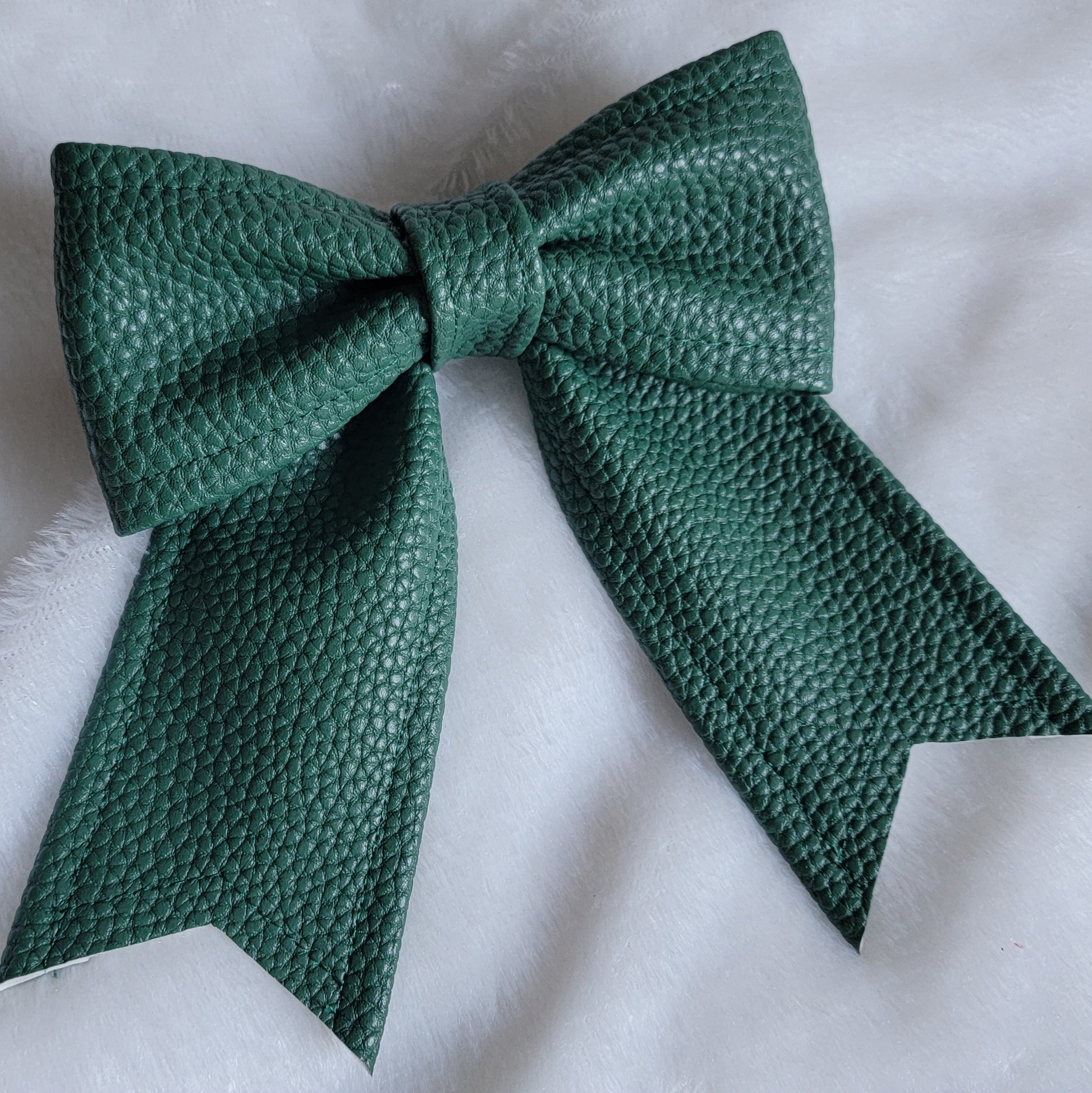 Dark green faux leather sailor bow displayed on a white fabric background.