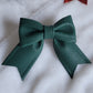 Dark green faux leather sailor bow displayed on a white fabric background.