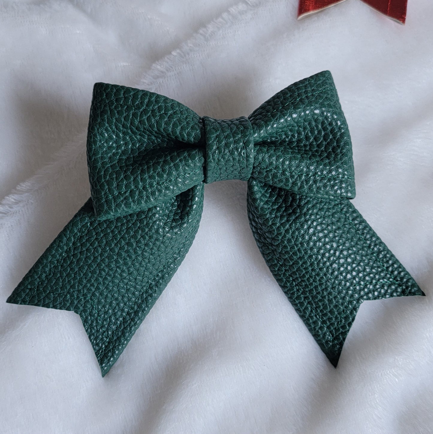 Dark green faux leather sailor bow displayed on a white fabric background.