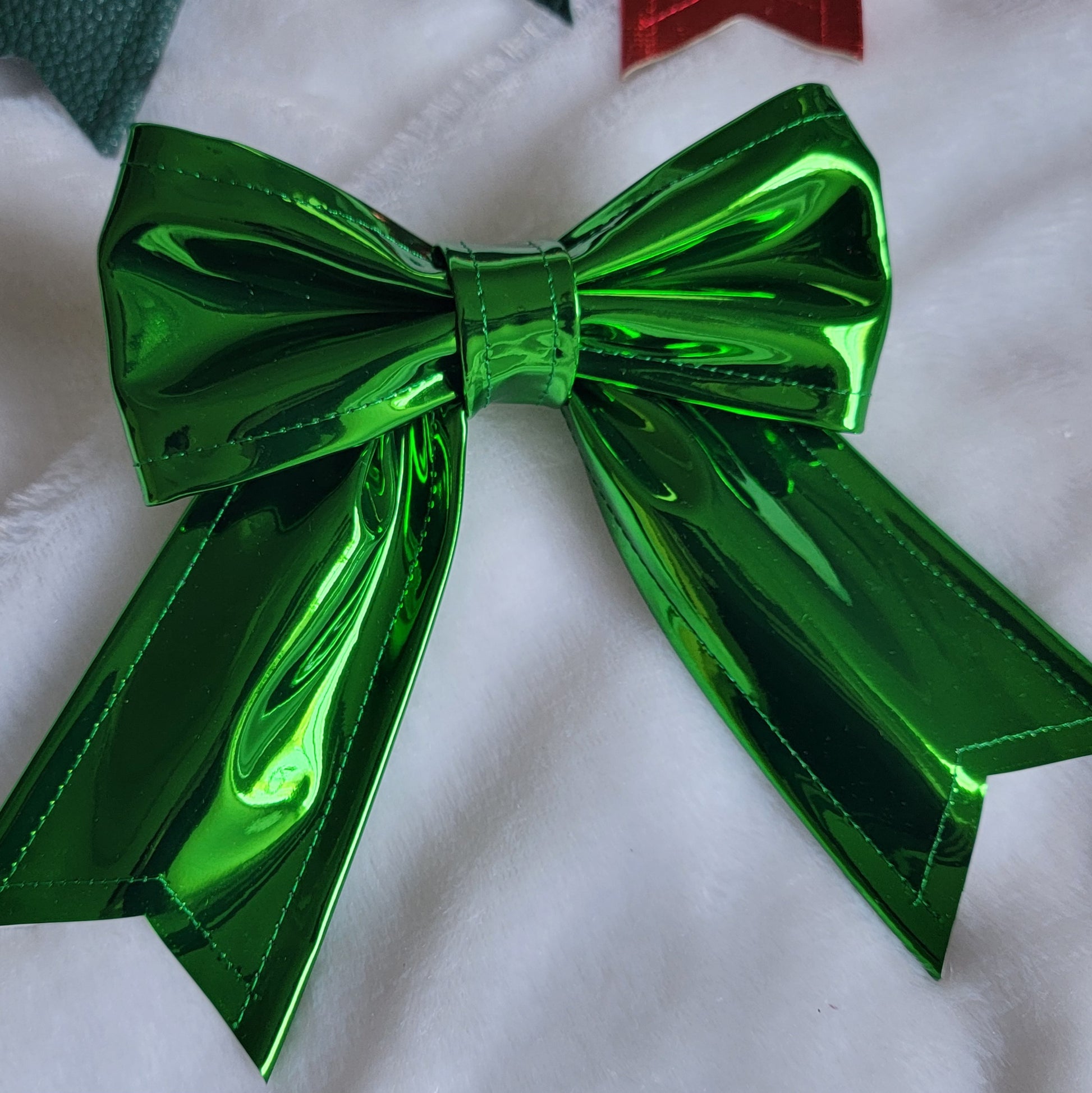 Green metallic faux leather sailor bow displayed on a white fabric background.