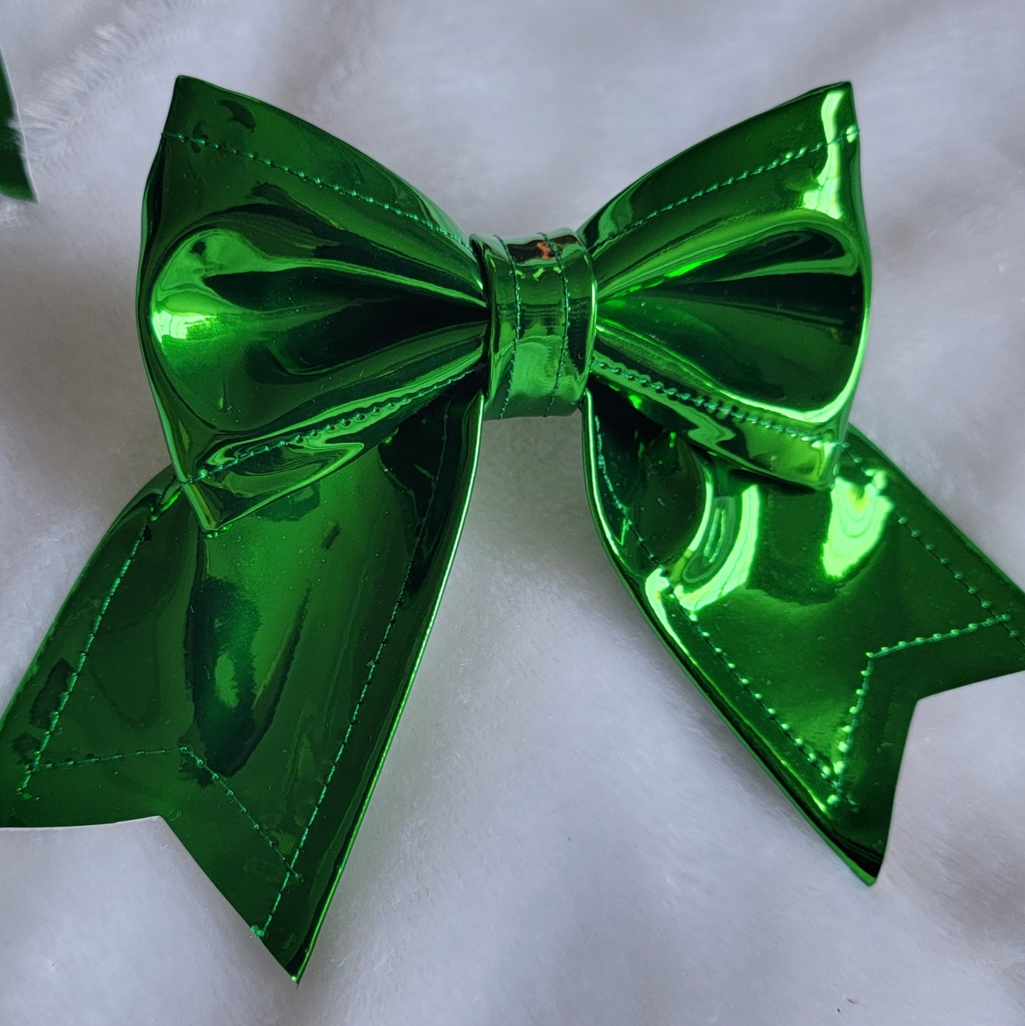 Green metallic faux leather sailor bow displayed on a white fabric background.