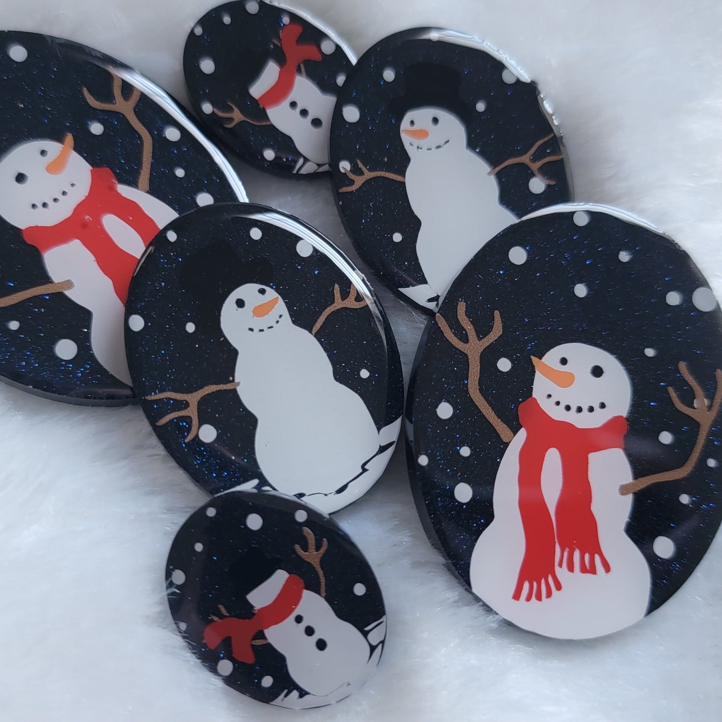 Six sparkly dark blue oval epoxy resin pieces in three different sizes, each with unique snowman scenes on them.
