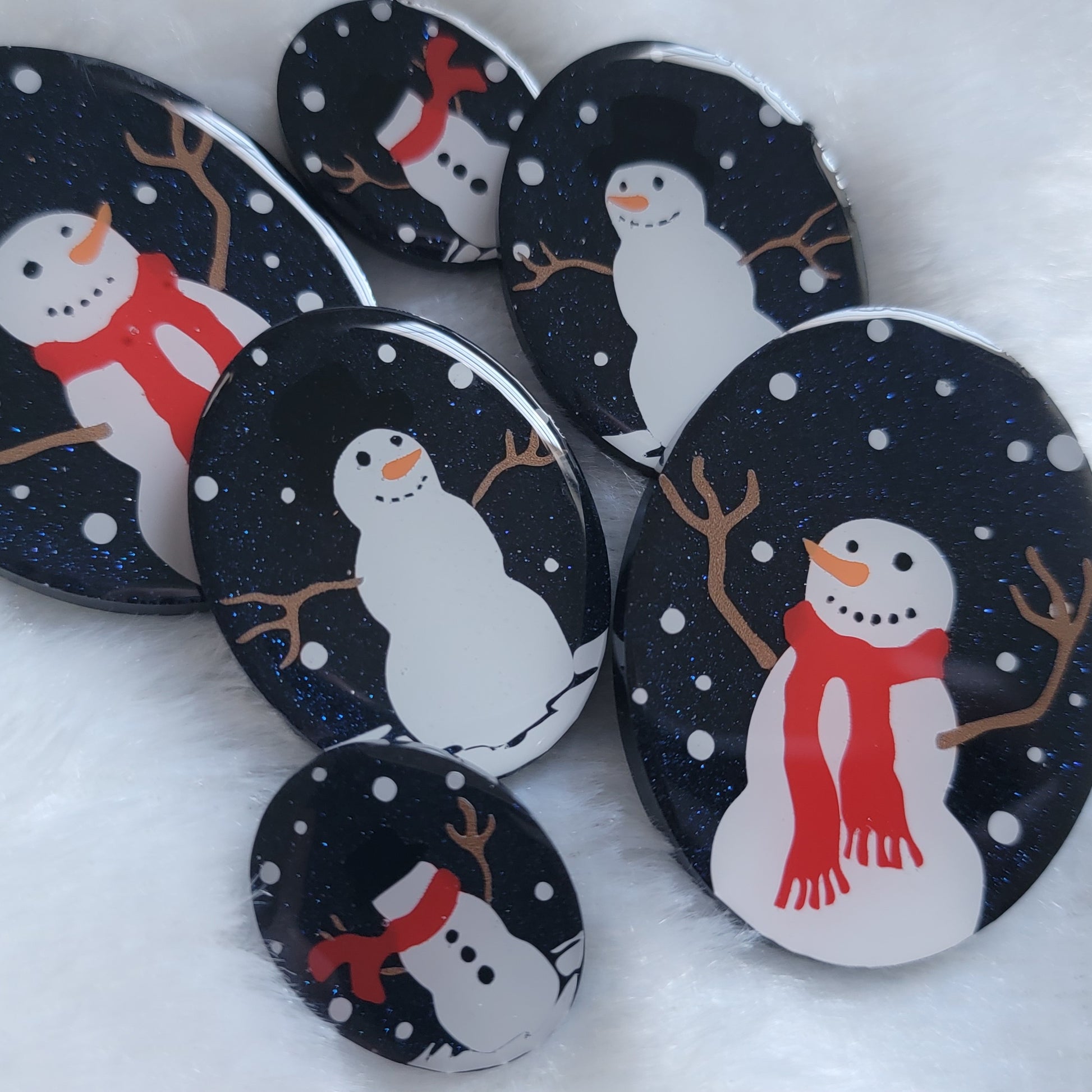 Six sparkly dark blue oval epoxy resin pieces in three different sizes, each with unique snowman scenes on them.