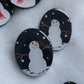 Two dark blue sparkly oval-shaped epoxy resin pieces with snowman designs, displayed on a white background
