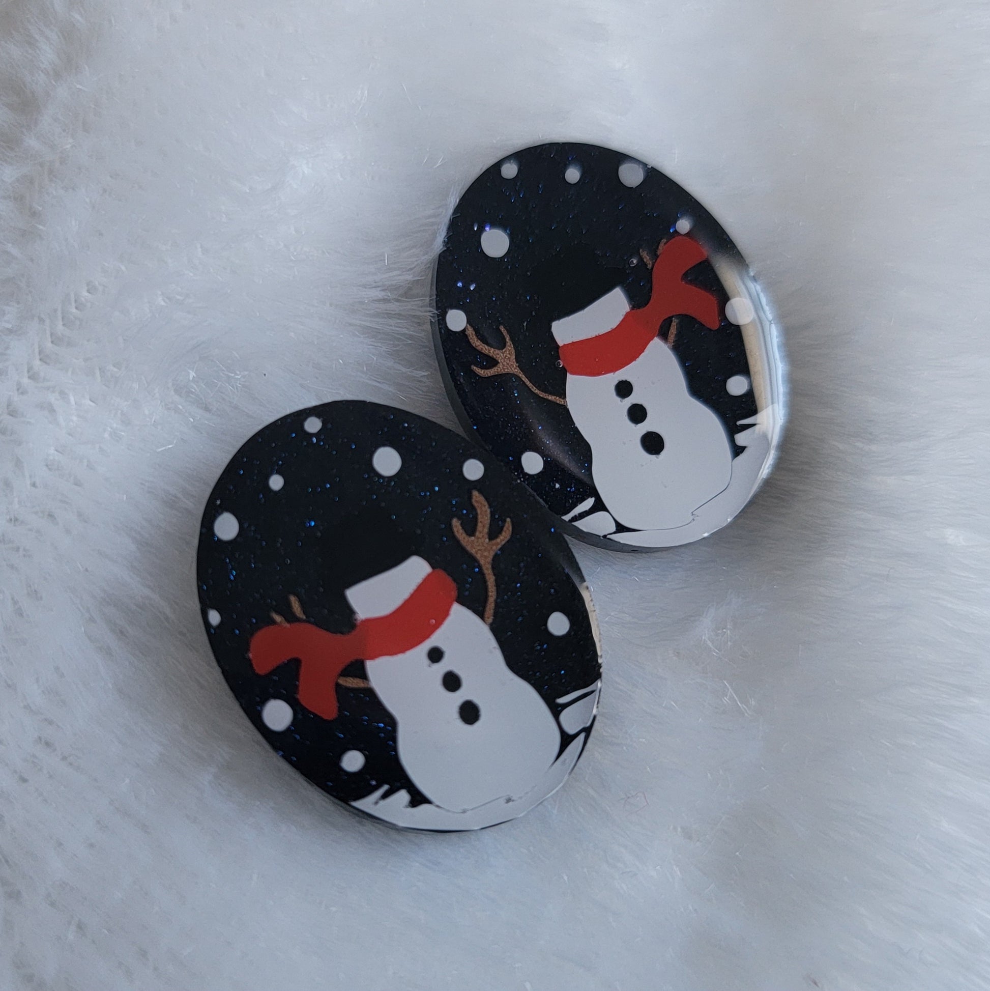 Two dark blue sparkly oval-shaped epoxy resin pieces with snowman designs, displayed on a white background