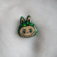 Labubu inspired small epoxy resin pet tag, made with green glitter and acrylic painted details.