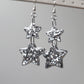 Drop earrings with star-shaped silver glitter epoxy resin pieces, displayed on a white earring hanger.