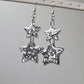 Drop earrings with star-shaped silver glitter epoxy resin pieces, displayed on a white earring hanger.