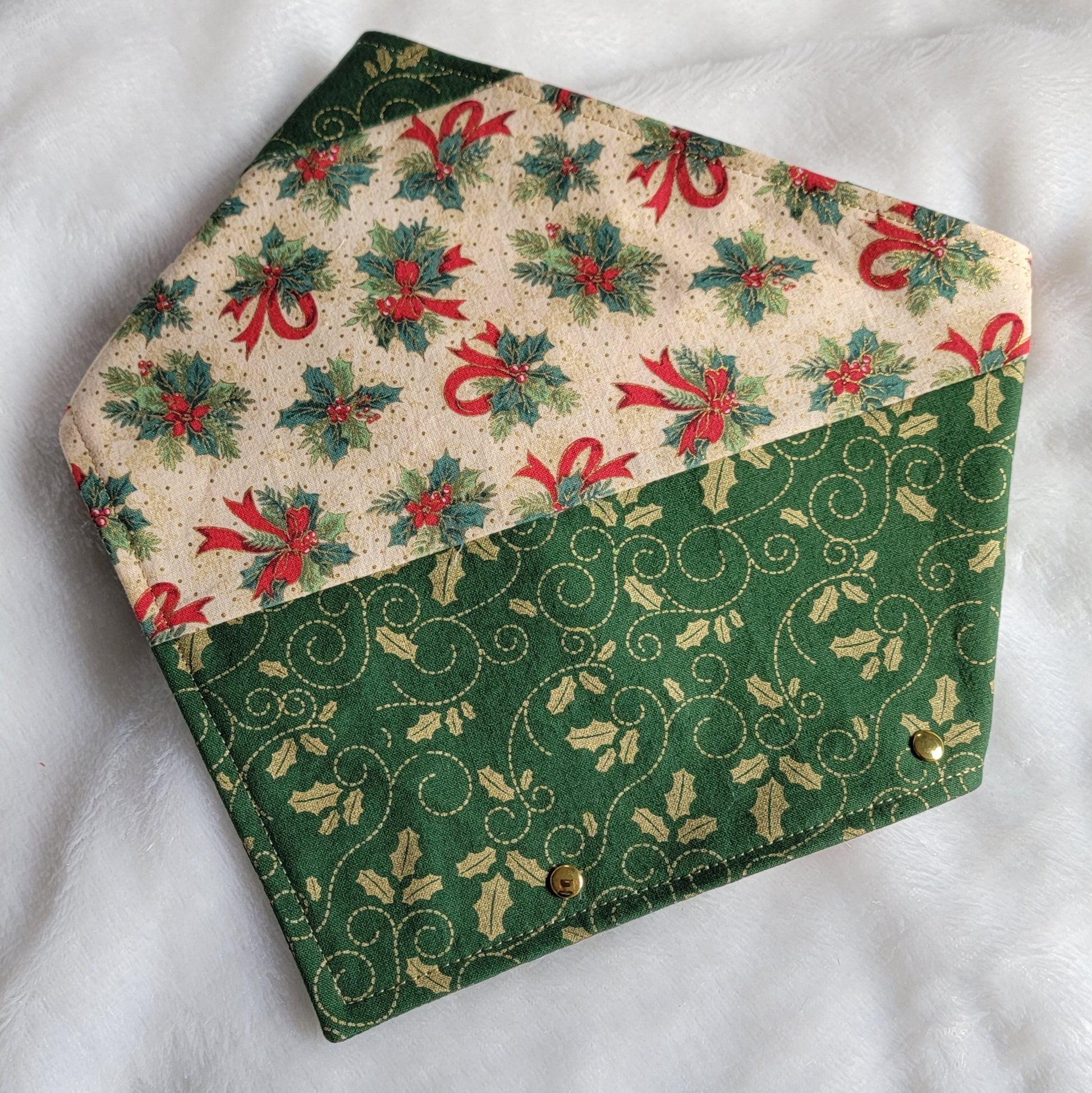 Handmade fabric pet bandana featuring stripes of Christmas holiday themed fabric in mistletoe prints, with gold colored metal rivets along one edge.