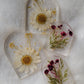Four arch shaped pieces of clear epoxy resin with flowers cast in them, two larger with white daisies and two smaller with purple blossoms.