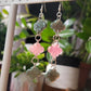 Long drop earrings made with epoxy resin quatrefoil charms, two green with crystal texture and one smooth pink charm in the center.