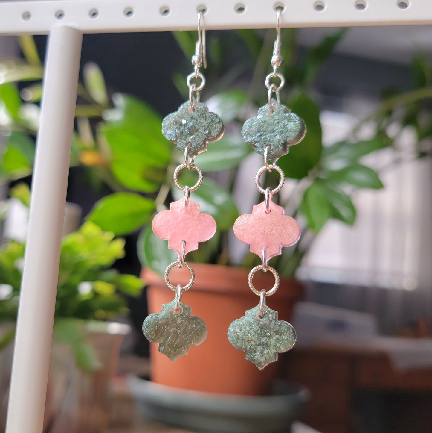 Long drop earrings made with epoxy resin quatrefoil charms, two green with crystal texture and one smooth pink charm in the center.
