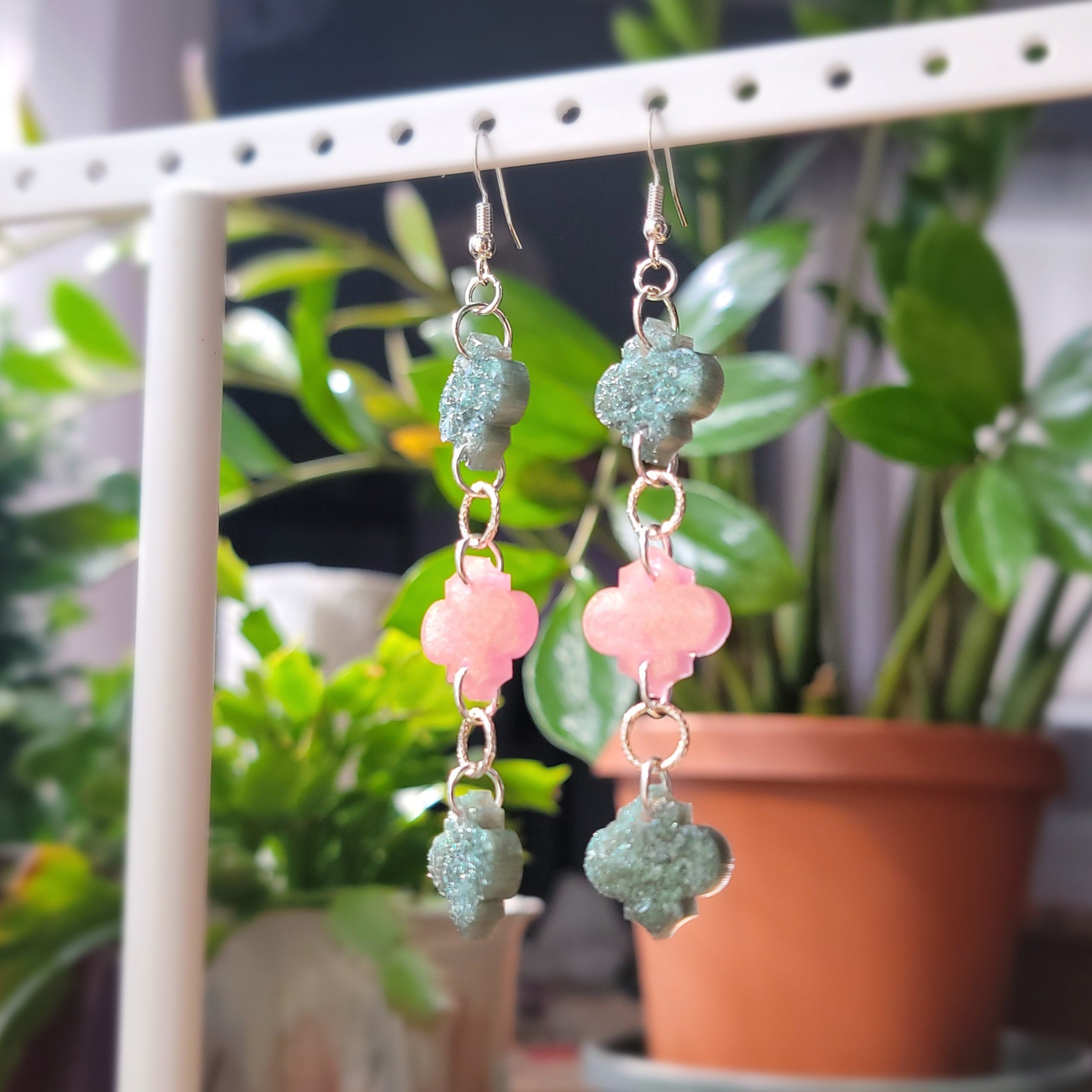 Long drop earrings made with epoxy resin quatrefoil charms, two green with crystal texture and one smooth pink charm in the center.