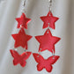 Three tiered drop earrings made from translucent red star and butterfly shaped epoxy resin pieces.