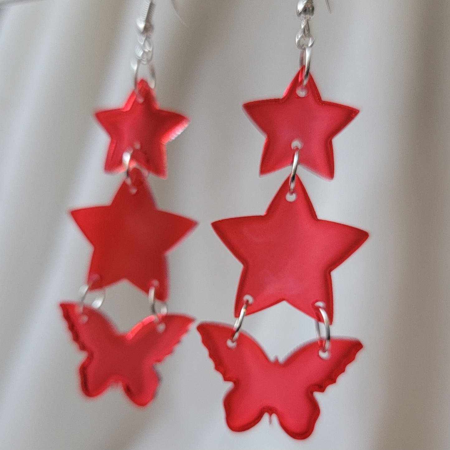 Three tiered drop earrings made from translucent red star and butterfly shaped epoxy resin pieces.