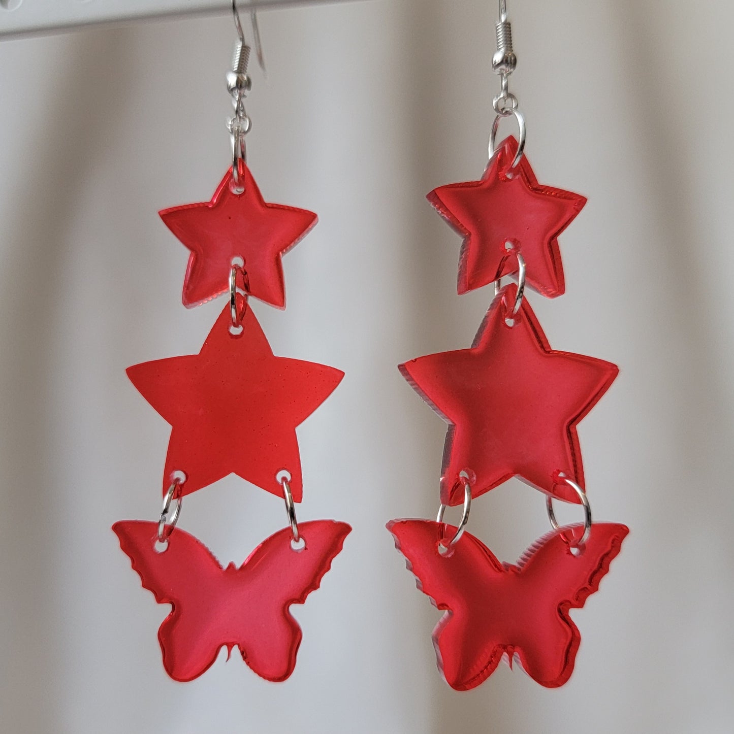 Three tiered drop earrings made from translucent red star and butterfly shaped epoxy resin pieces.