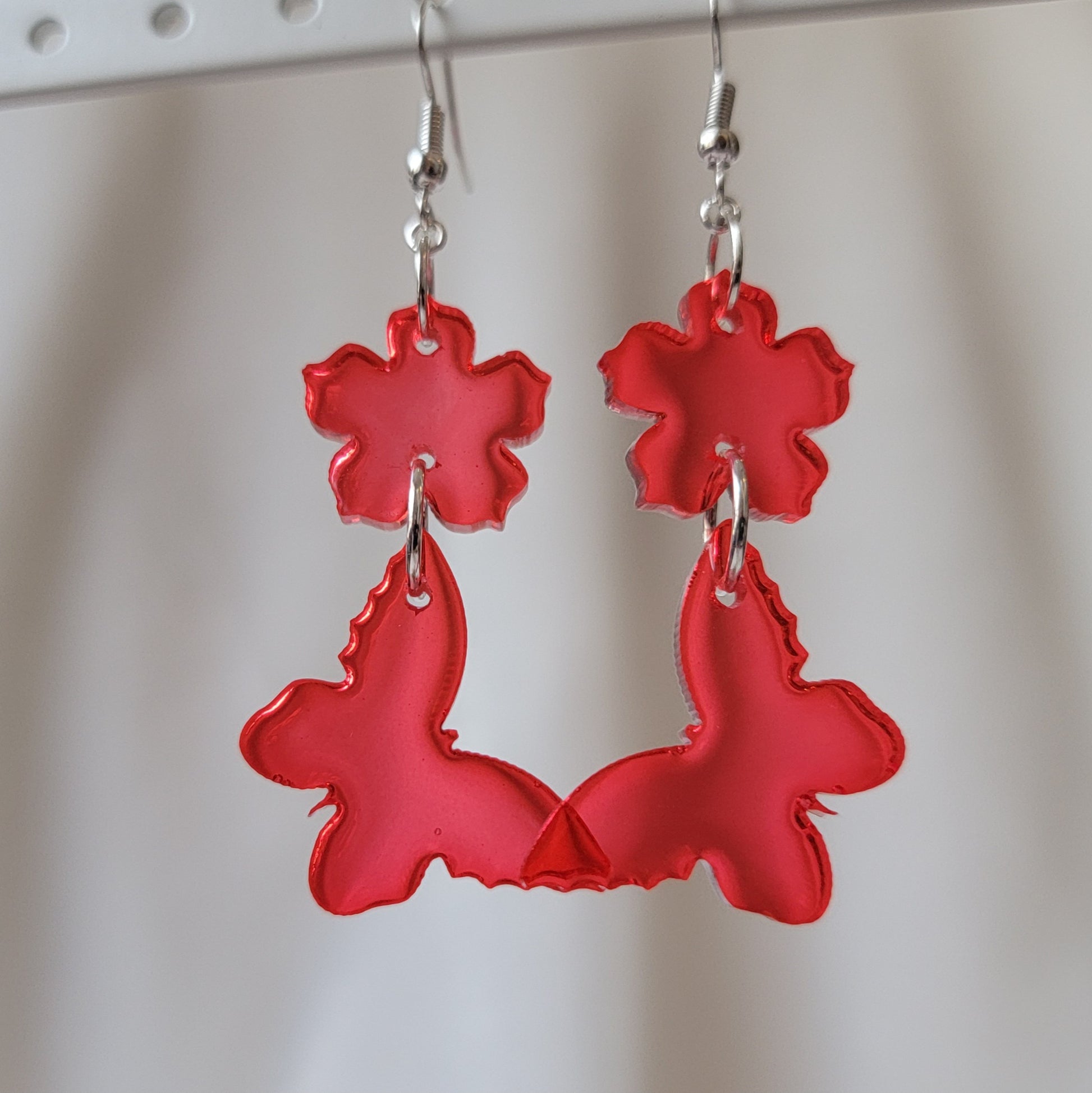 Two tiered drop earrings made from translucent red flower and butterfly shaped epoxy resin pieces.