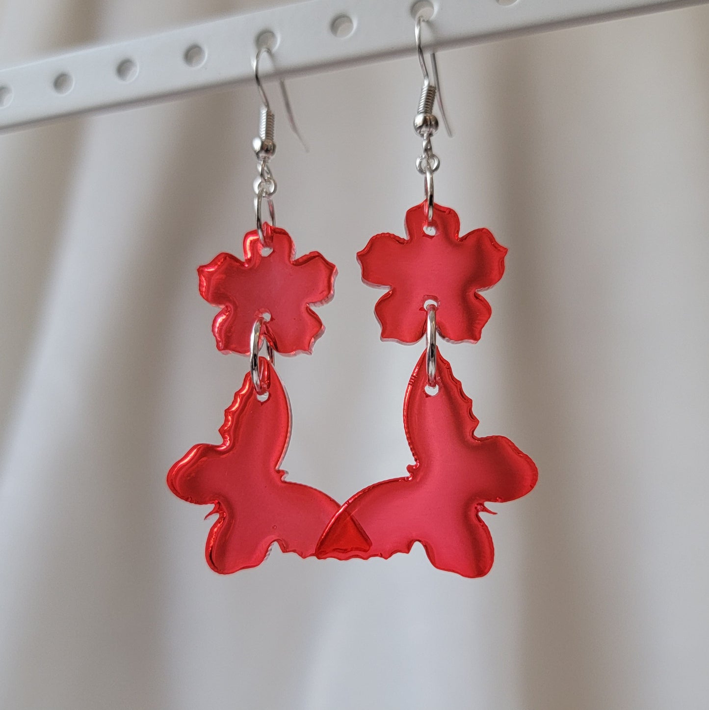 Two tiered drop earrings made from translucent red flower and butterfly shaped epoxy resin pieces.