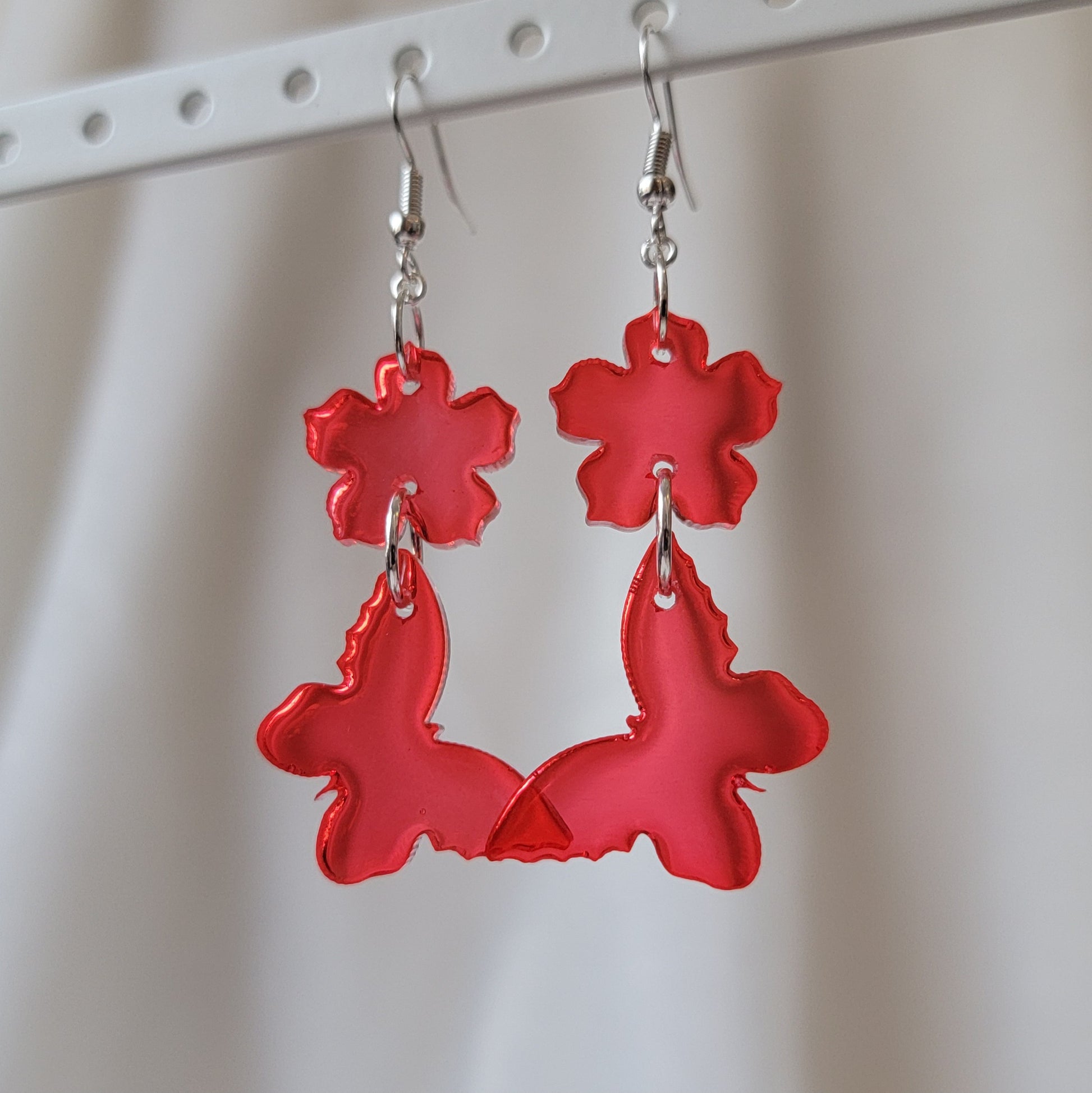 Two tiered drop earrings made from translucent red flower and butterfly shaped epoxy resin pieces.