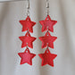 Three tiered drop earrings made from translucent red star shaped epoxy resin pieces.