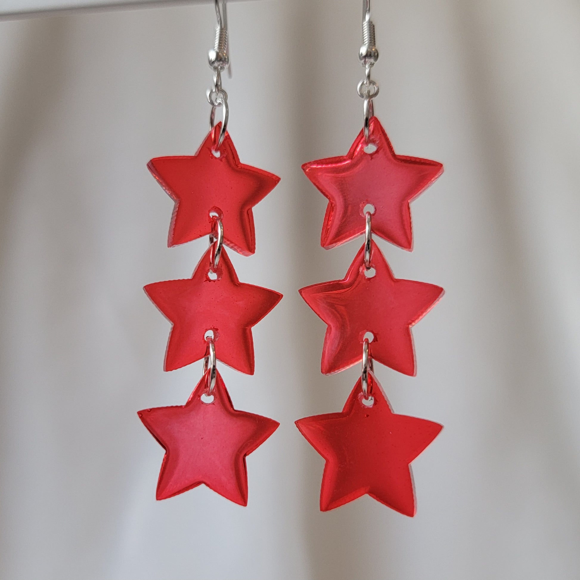 Three tiered drop earrings made from translucent red star shaped epoxy resin pieces.