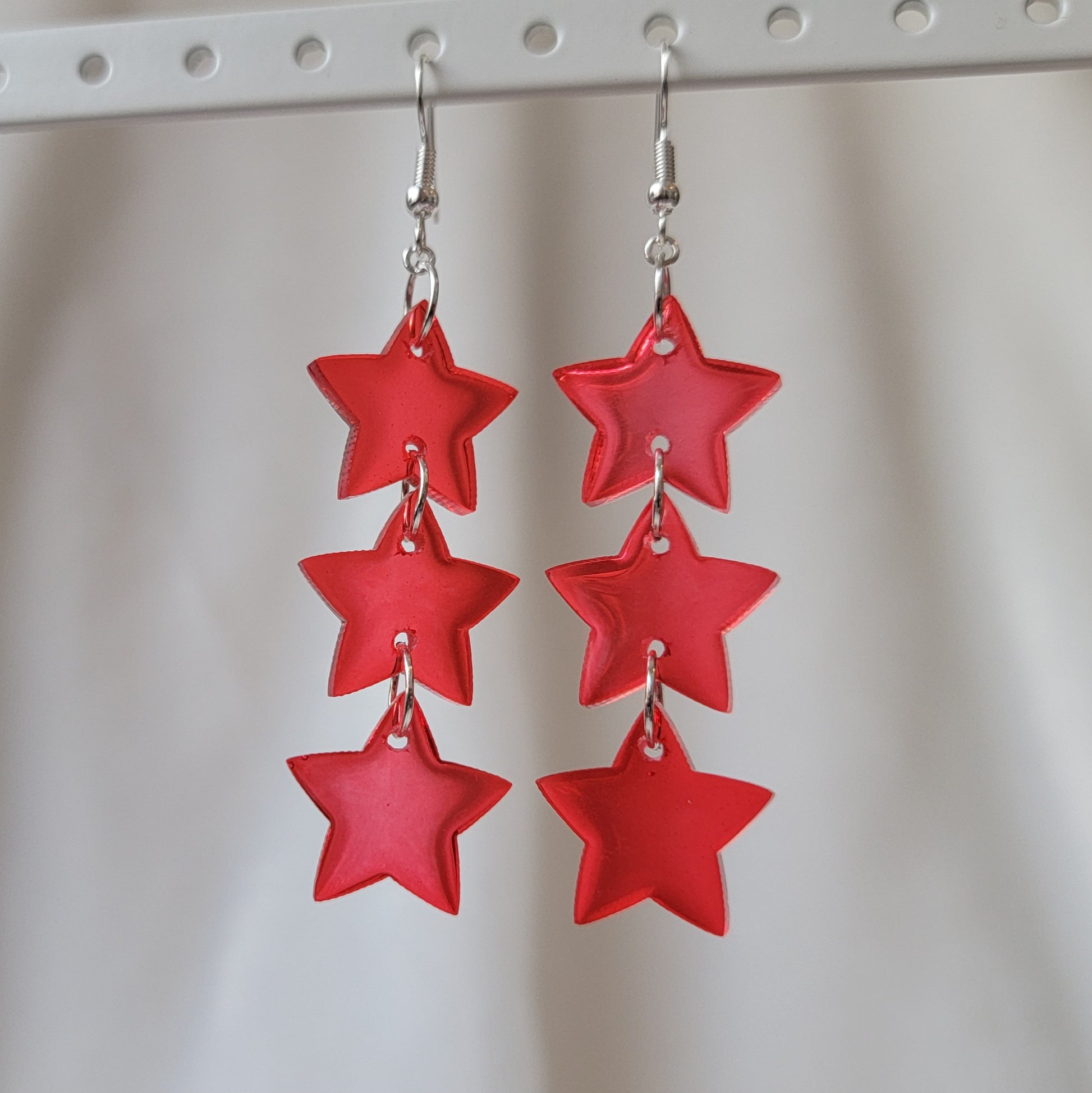 Three tiered drop earrings made from translucent red star shaped epoxy resin pieces.