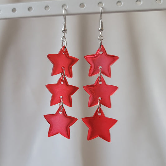 Three tiered drop earrings made from translucent red star shaped epoxy resin pieces.