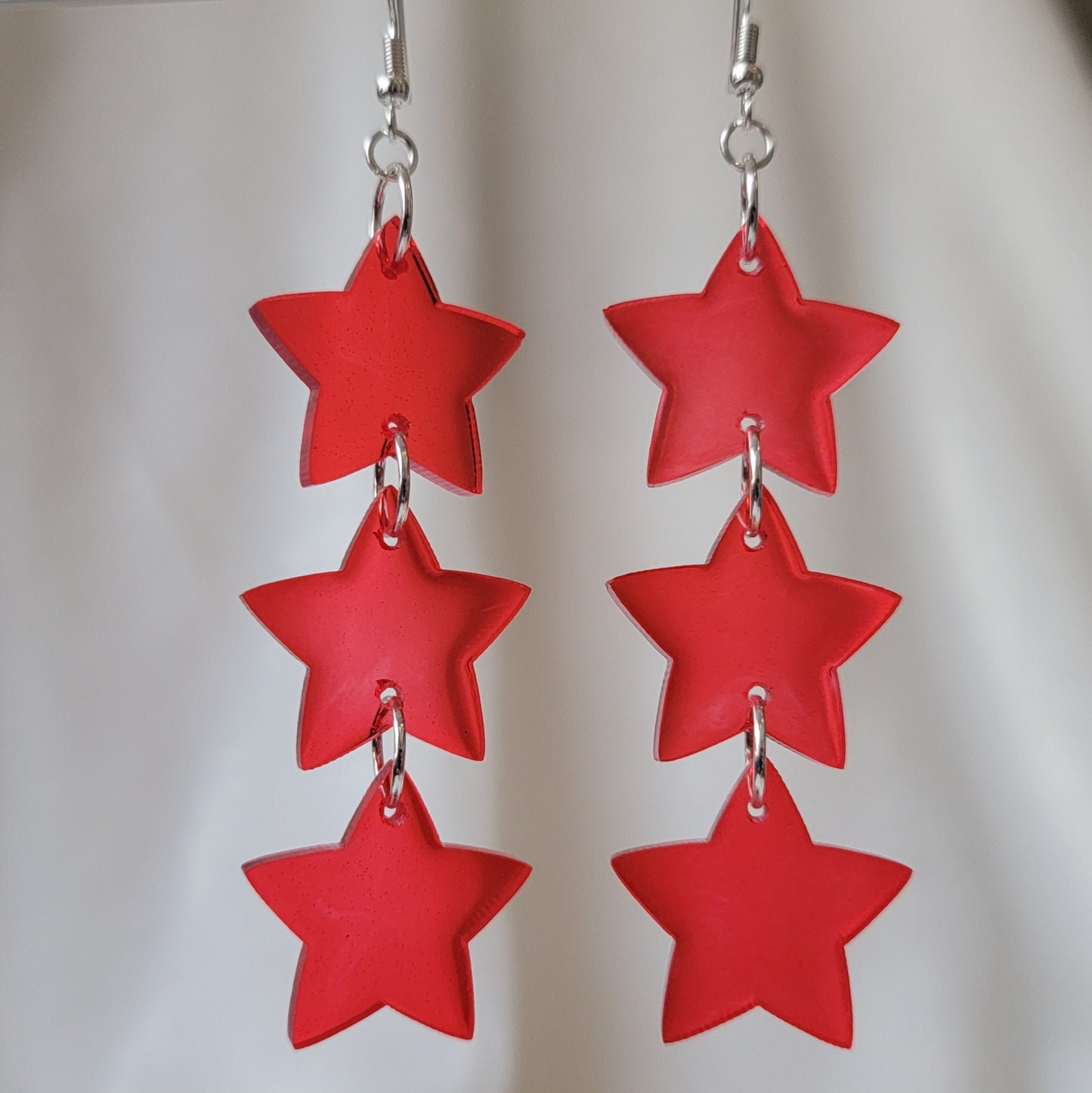 Three tiered drop earrings made from translucent red star shaped epoxy resin pieces.