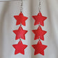 Three tiered drop earrings made from translucent red star shaped epoxy resin pieces.