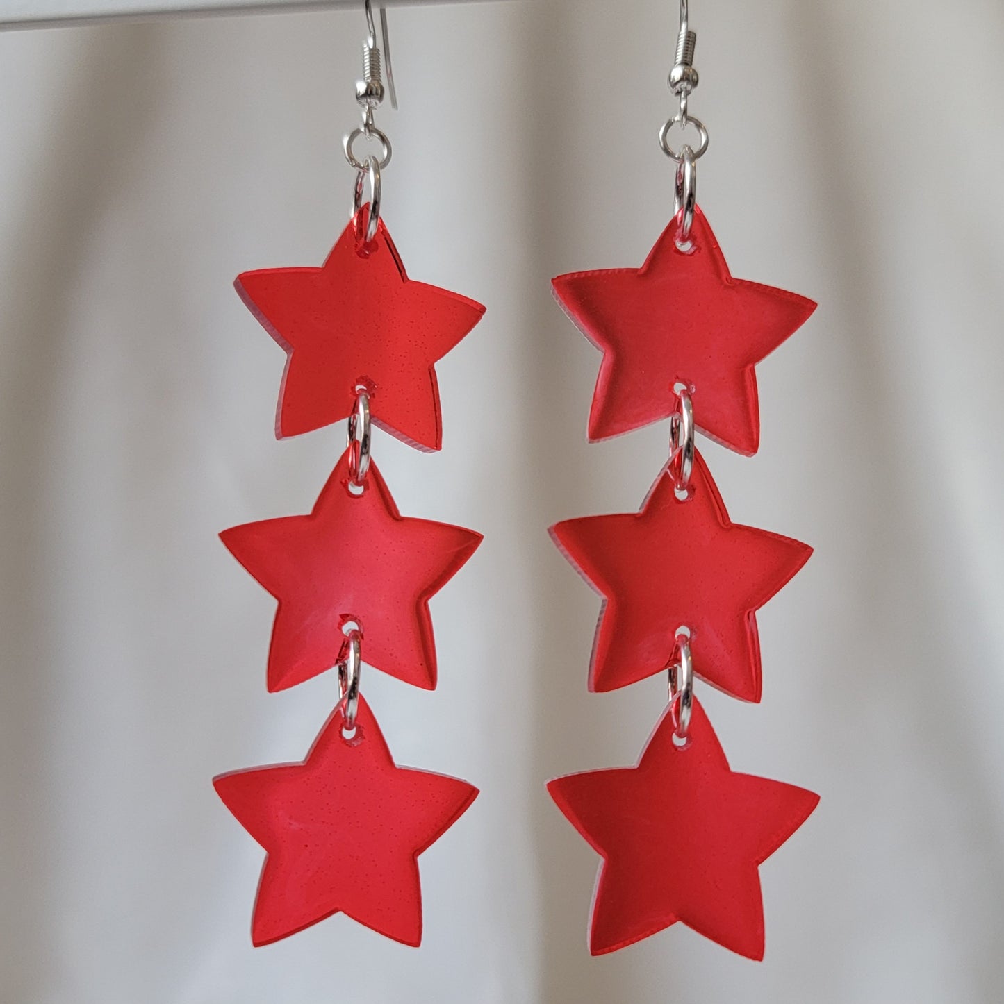 Three tiered drop earrings made from translucent red star shaped epoxy resin pieces.