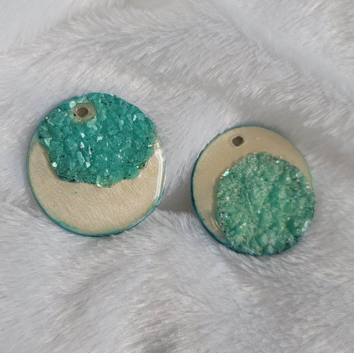 Two round charms made of wood sealed in resin, with aqua green resin crystals placed to create a crescent moon shape.