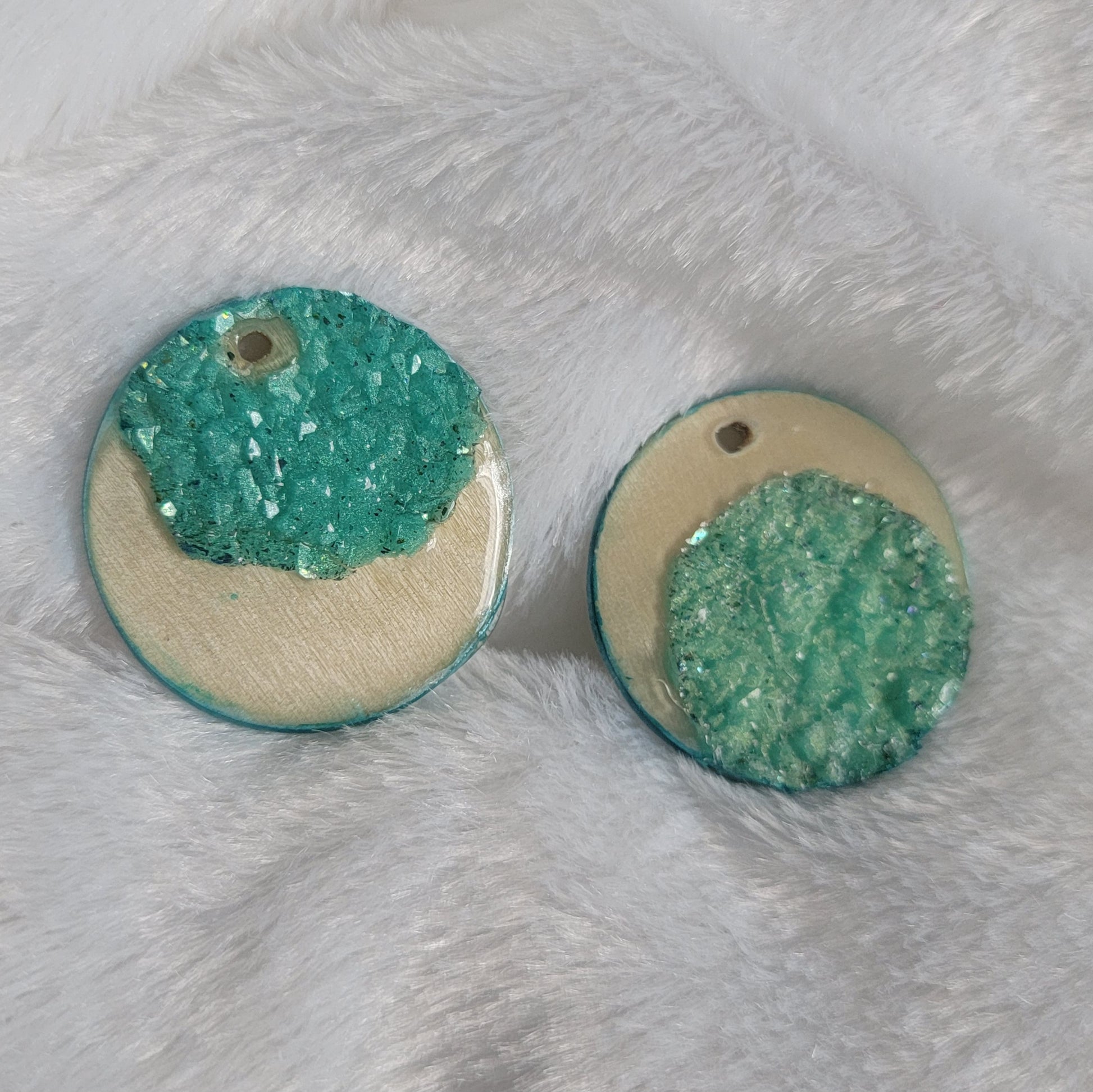 Two round charms made of wood sealed in resin, with aqua green resin crystals placed to create a crescent moon shape.