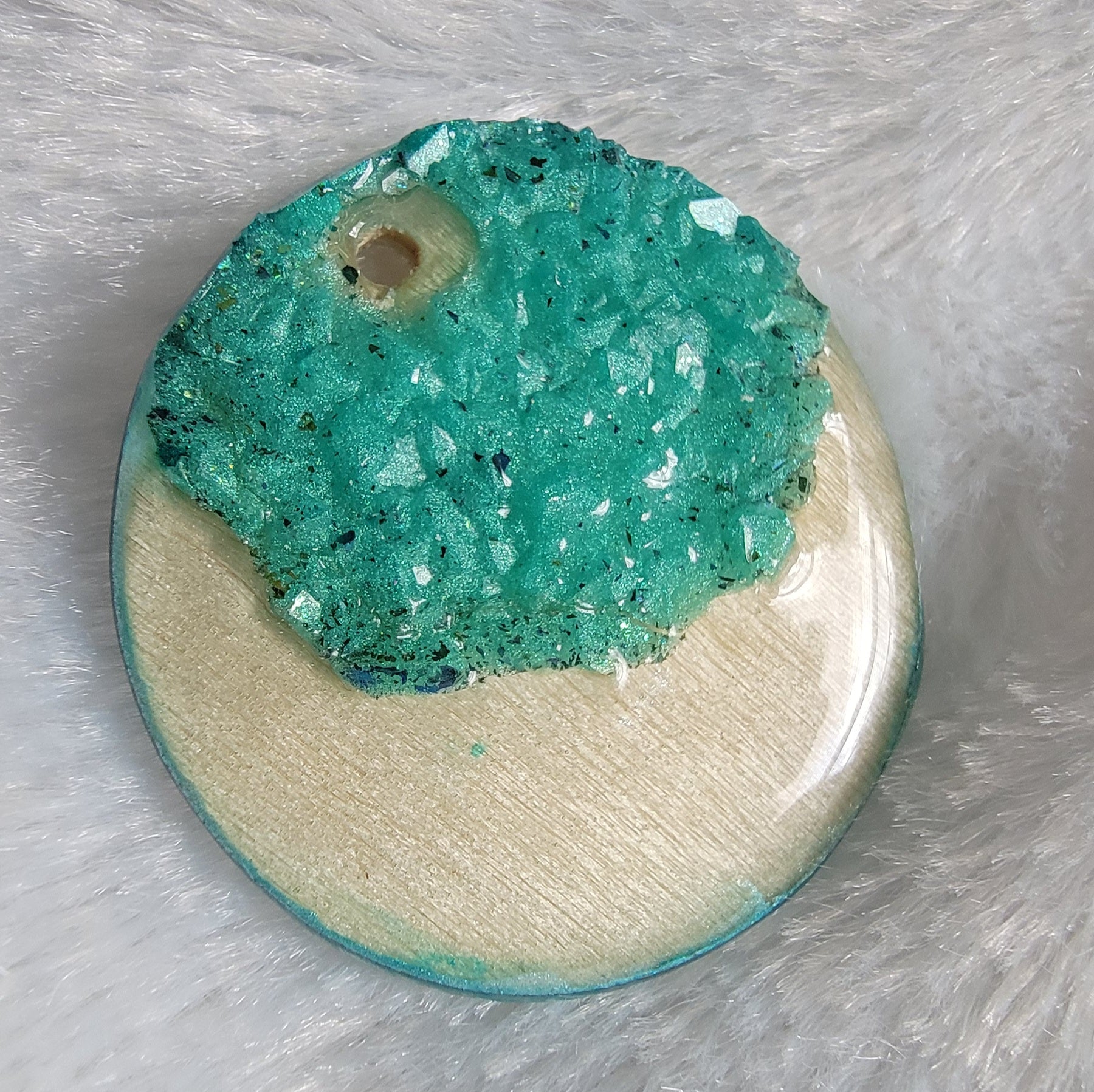Round charm made of wood sealed in resin, with aqua green resin crystals placed to create a crescent moon shape.