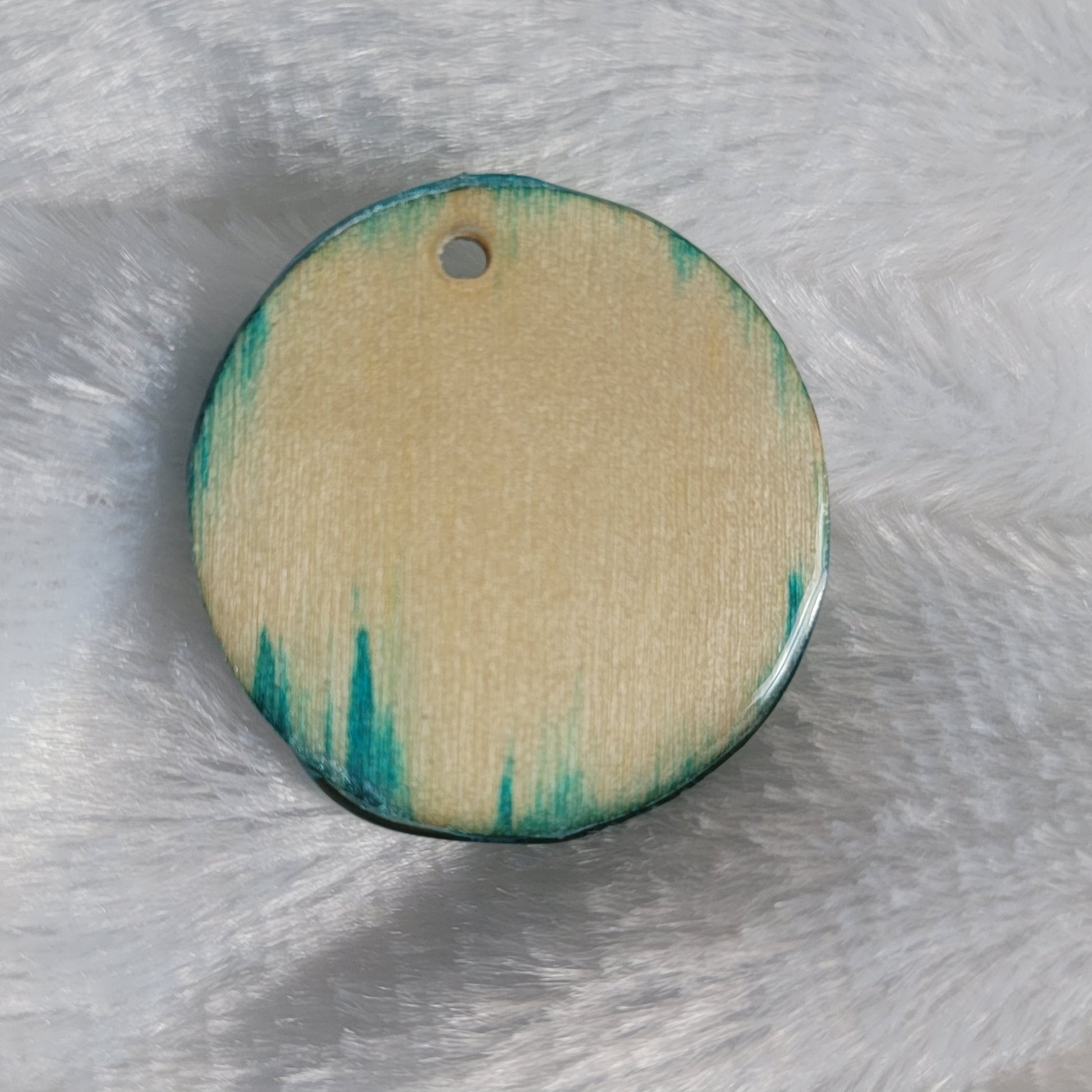 Round charm made of wood sealed in resin, with aqua blue ink fading into the woodgrain of the edges.