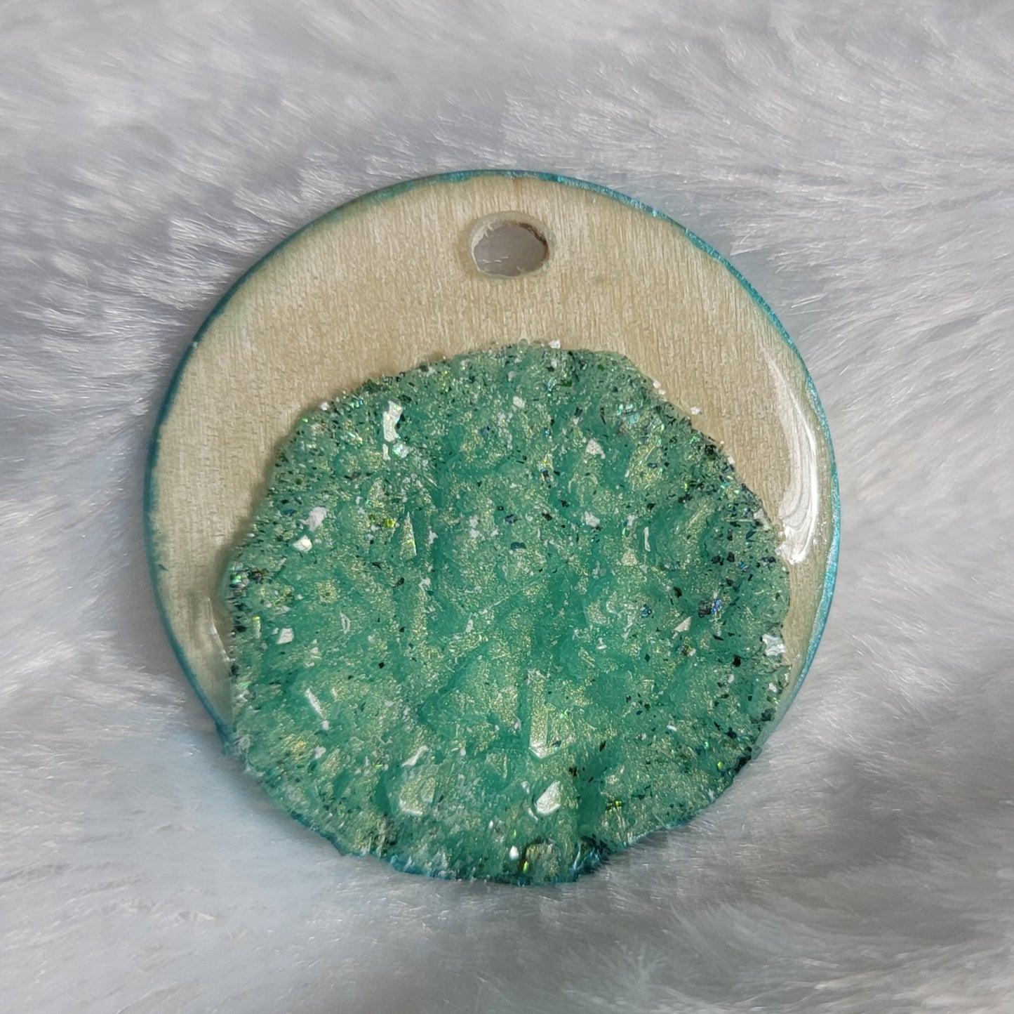 Round charm made of wood sealed in resin, with aqua green resin crystals placed to create a crescent moon shape.