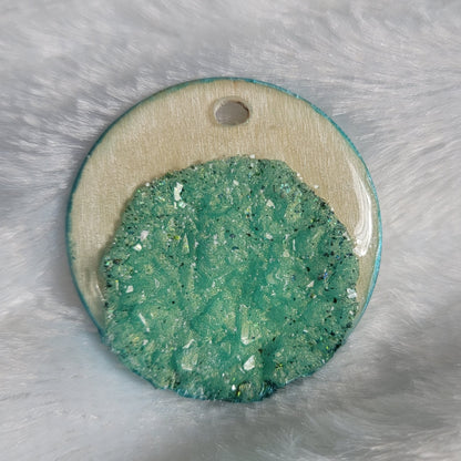Round charm made of wood sealed in resin, with aqua green resin crystals placed to create a crescent moon shape.