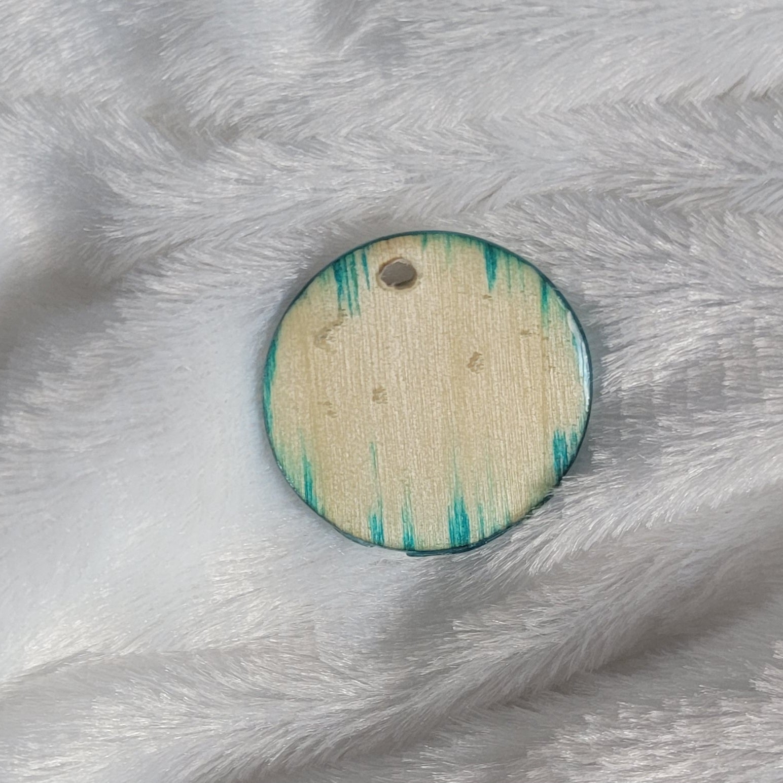 Round charm made of wood sealed in resin, with aqua blue ink fading into the woodgrain of the edges.