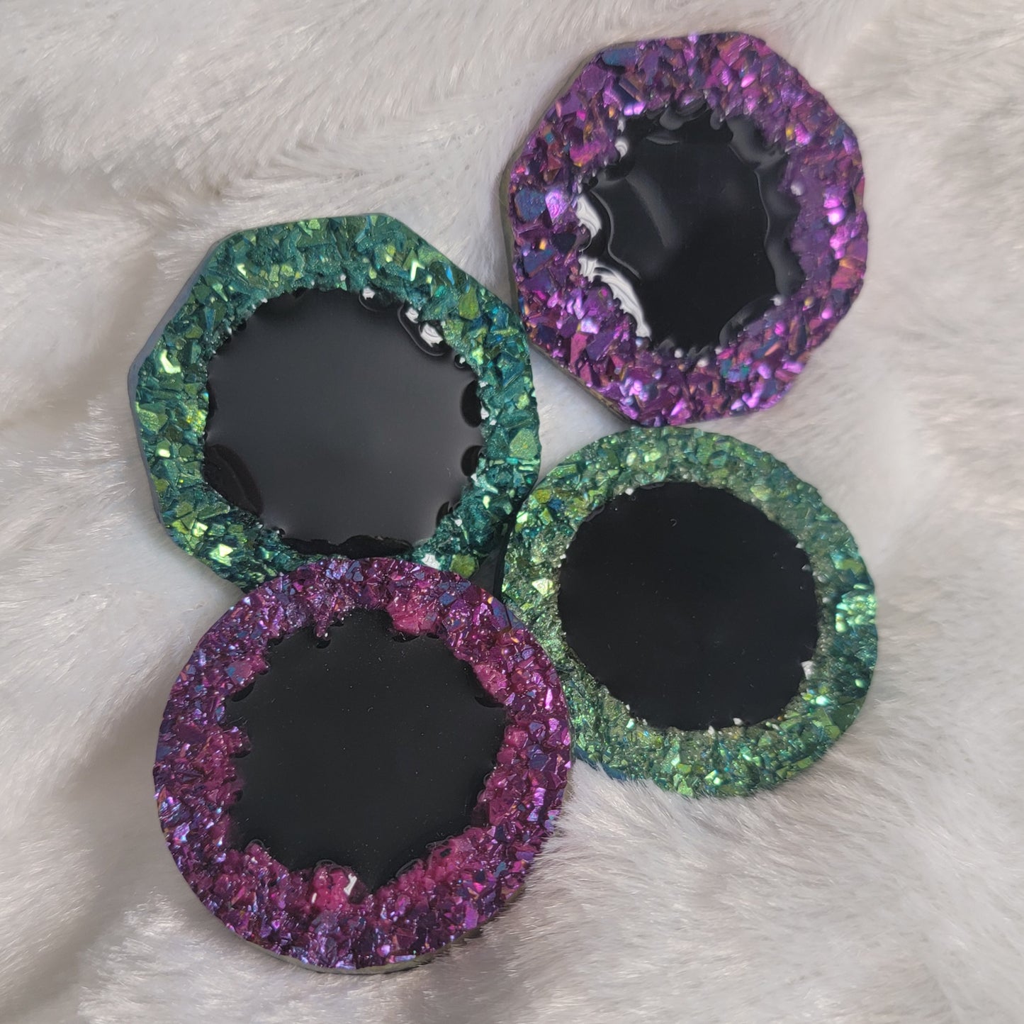Four epoxy resin pieces with crystal texture edges, two green and two purple, with black centers.